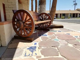 Un carro de madera con ruedas grandes, situado sobre un pavimento de baldosas con un muro de piedra al fondo.