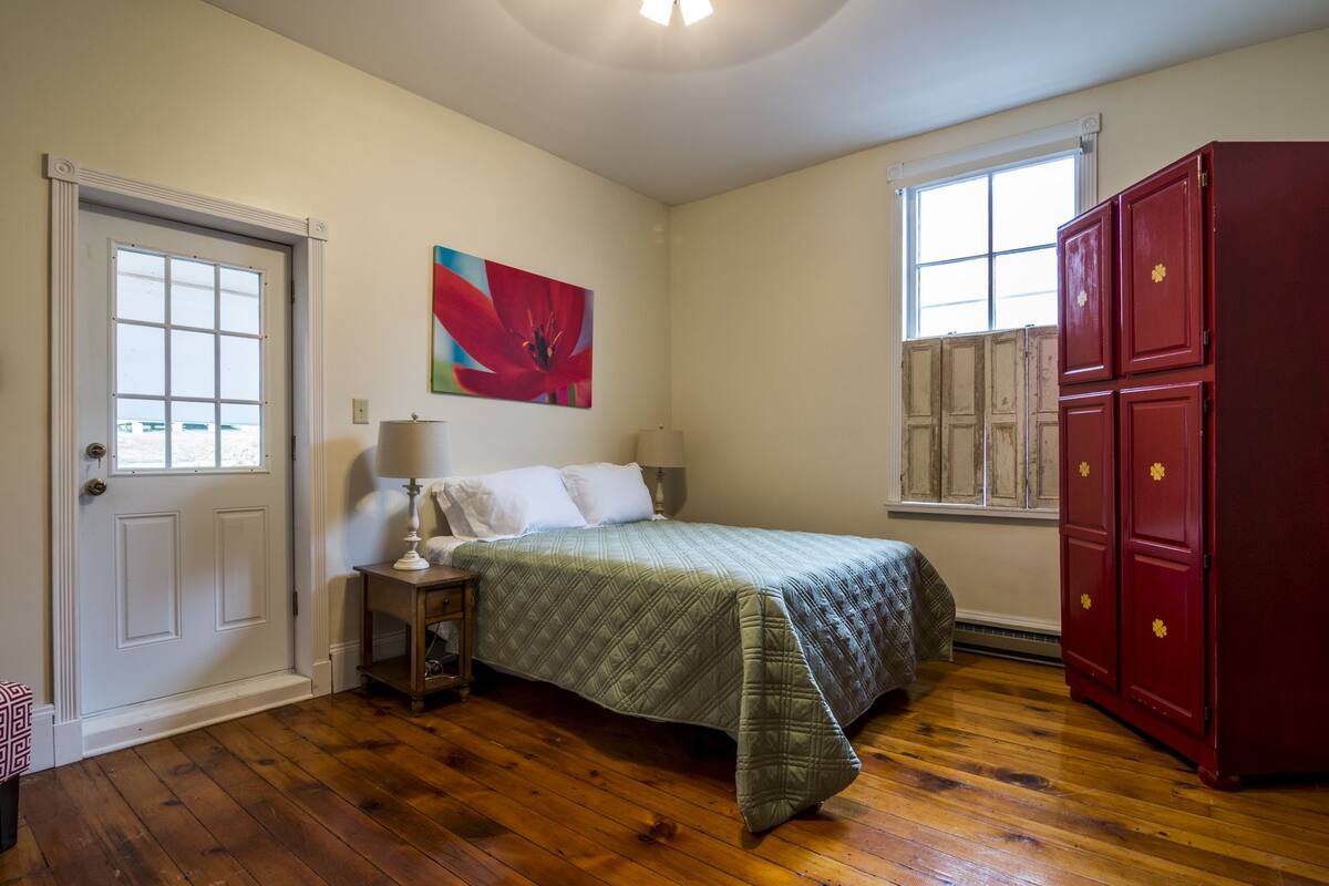 A bedroom with a bed, a nightstand, a red wardrobe, a window, and a door.