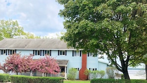 A light blue building with a red chimney, surrounded by a white picket fence and a well-maintained lawn. - Churchill Pointe Inn (Hubbard Lake)
