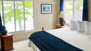 A bedroom with a large bed, two windows, a nightstand, a lamp, and a framed picture on the wall. - Churchill Pointe Inn (Hubbard Lake)