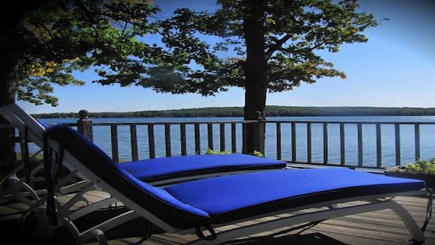 A wooden deck with a blue lounge chair and a wooden railing overlooking a lake. - Churchill Pointe Inn (Hubbard Lake)