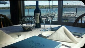 A table set with a bottle of wine, two wine glasses, a candle holder, and a menu. - Churchill Pointe Inn (Hubbard Lake)