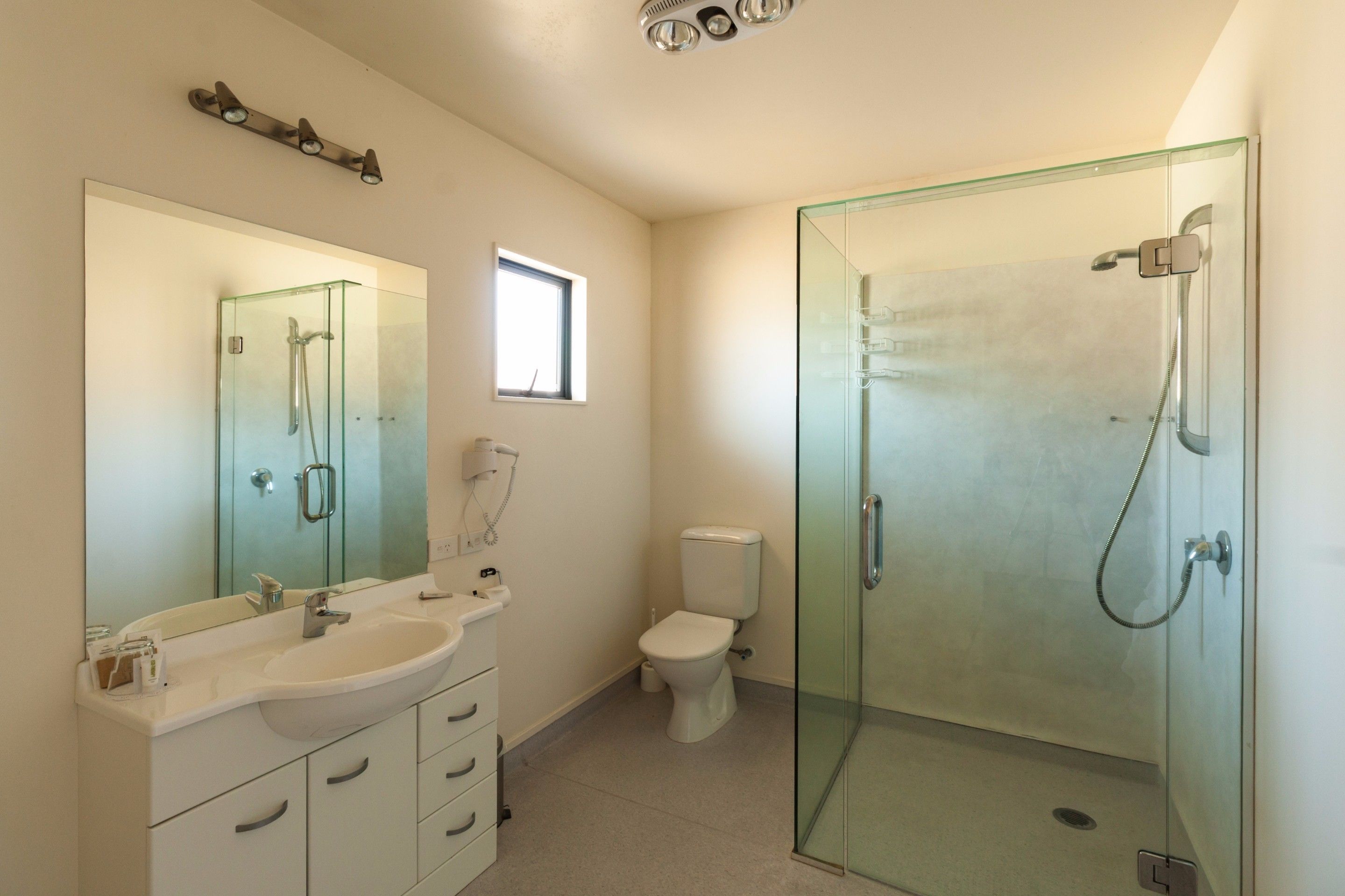 A modern bathroom with a glass-enclosed shower, a large mirror, and a white sink.