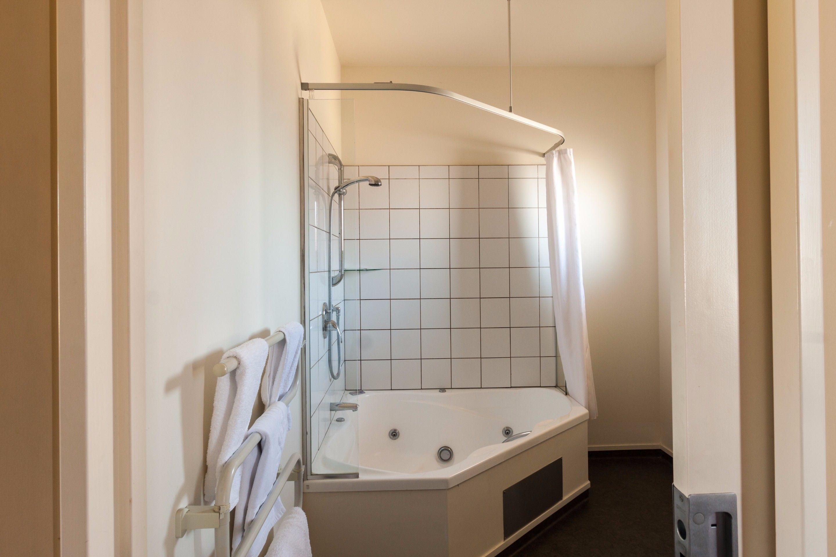 Un baño pequeño y moderno con cabina de ducha, bañera con mampara de vidrio y un perchero para toallas.
