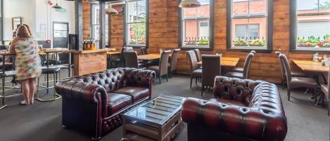 A spacious indoor area with leather sofas, tables, and chairs. There are large windows with views of the outside.