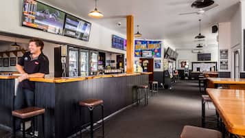 A bar area with a counter, stools, and a television screen displaying sports.