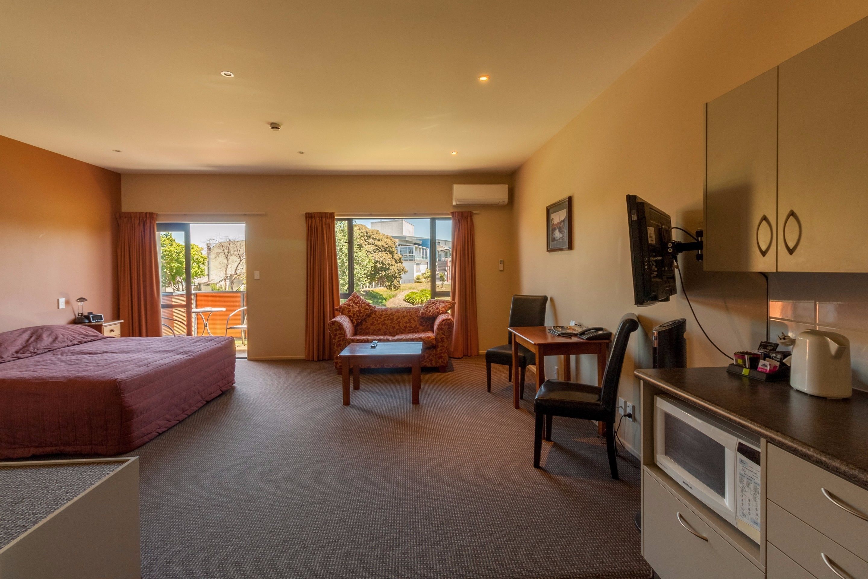 Habitación de hotel con cama, sofá, mesa de comedor, silla, televisión, microondas y ventana con cortinas.