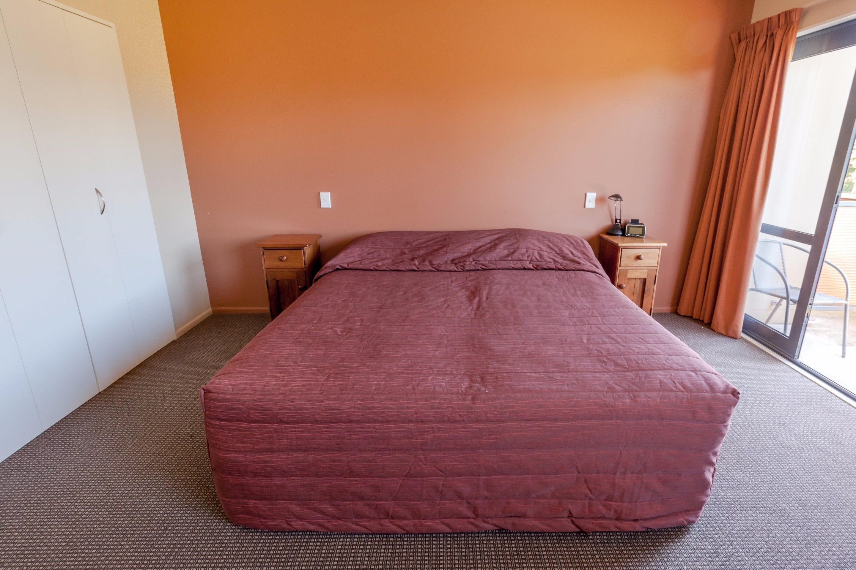 A hotel room with a large bed, two bedside tables, a nightstand, and a sliding glass door to the balcony.