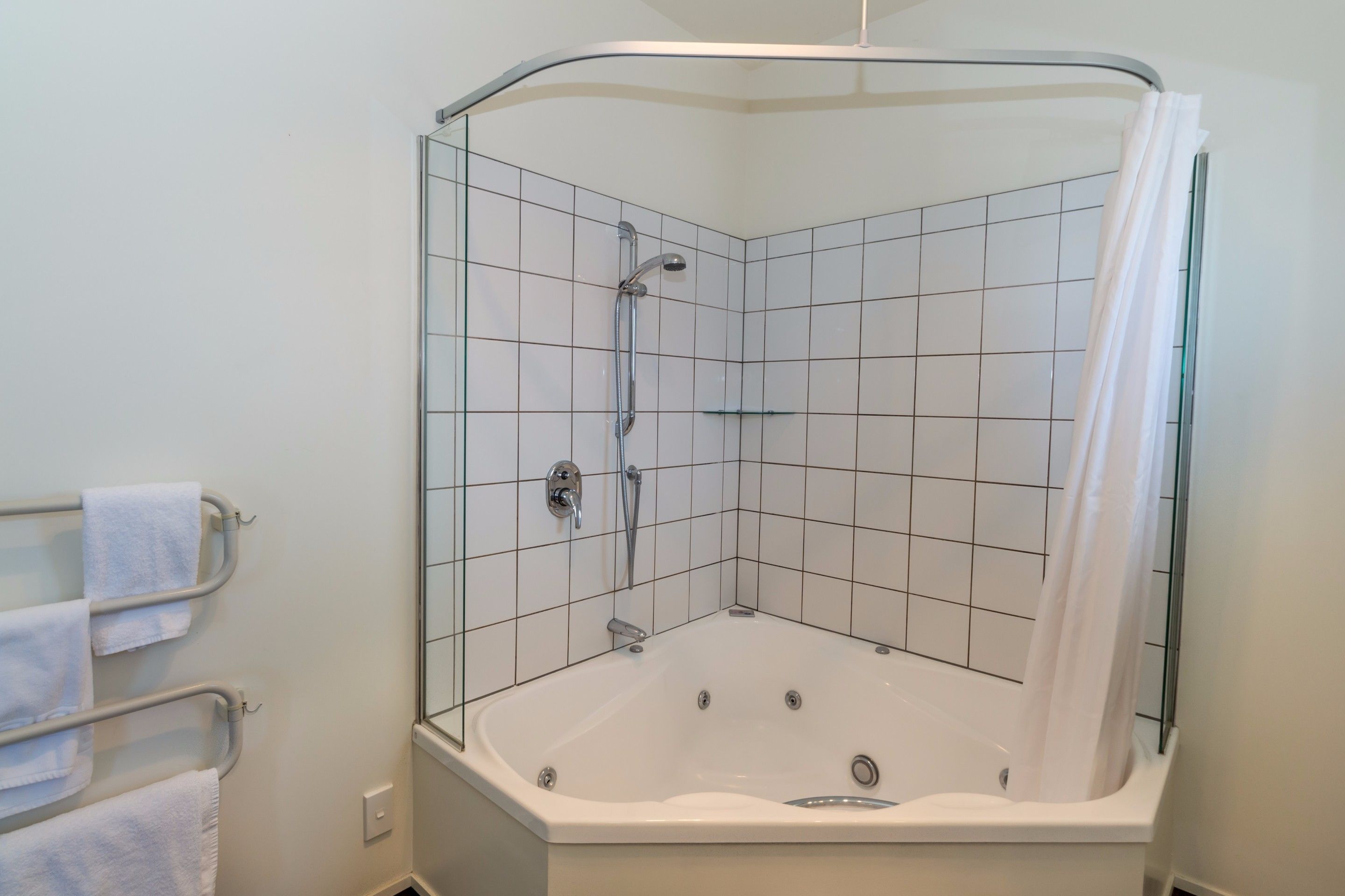 A corner shower with a glass enclosure, a white bathtub, and a towel rack with towels.