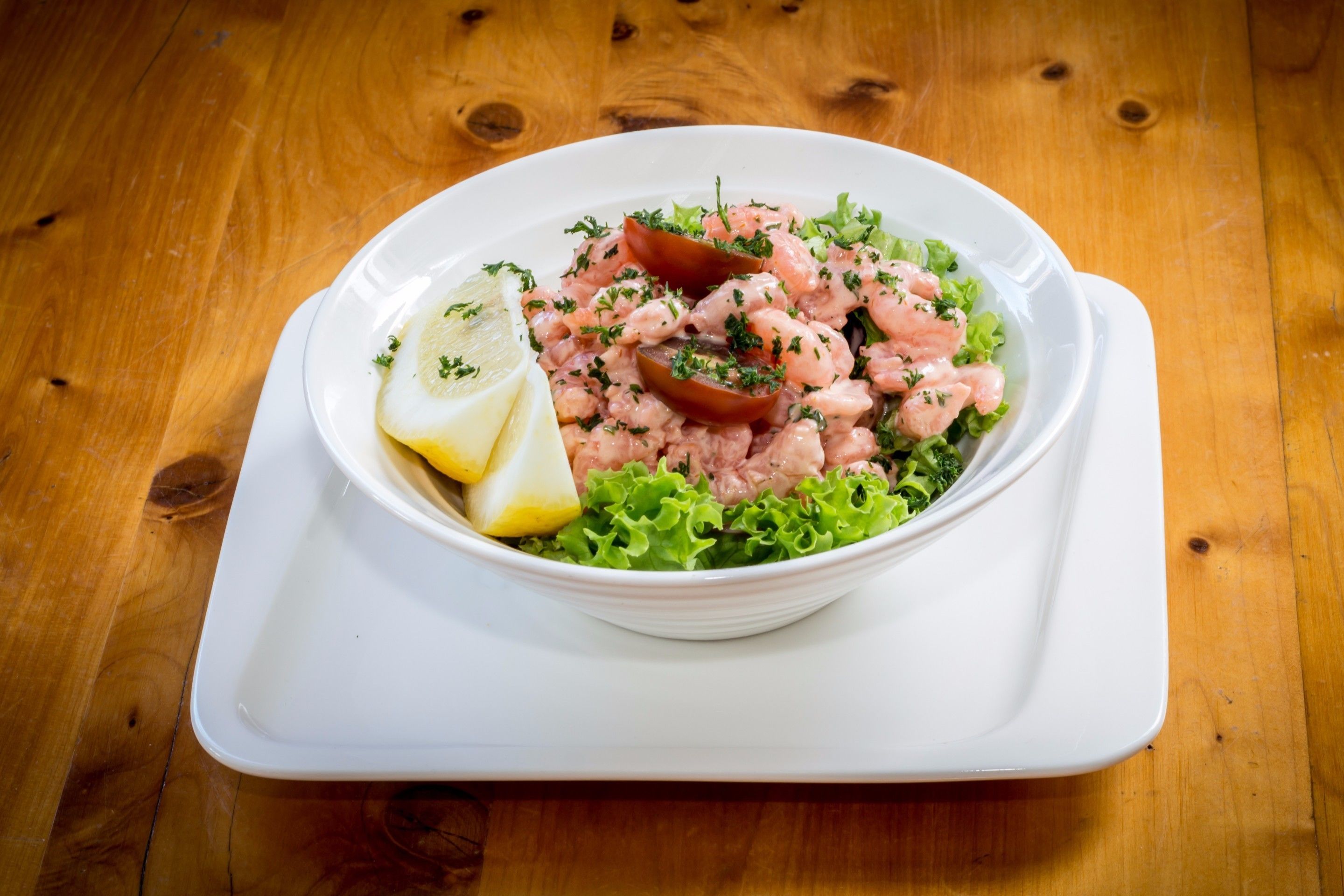 Un saladier blanc rempli de salade de crevettes, posé sur une table en bois.