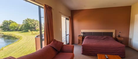 A hotel room with a large window, a sofa, a bed, and a small table.