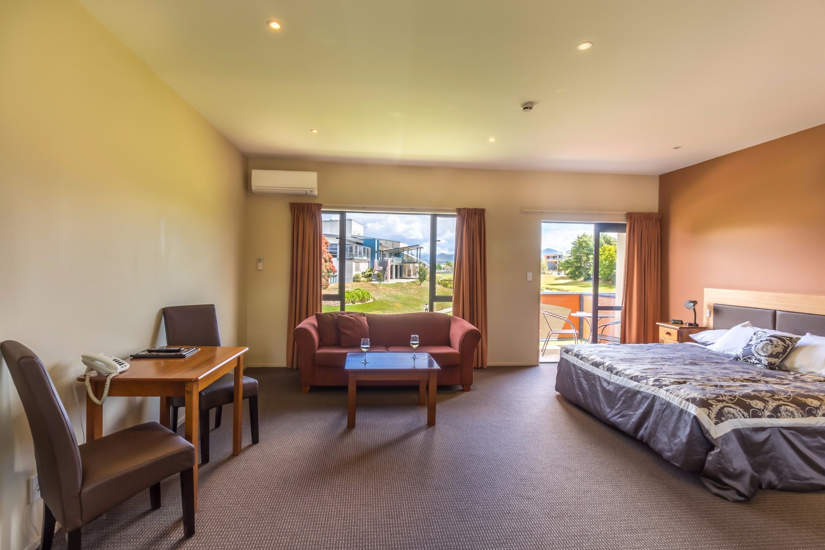A hotel room with a bed, a sofa, a desk with a phone, and a table with two glasses.