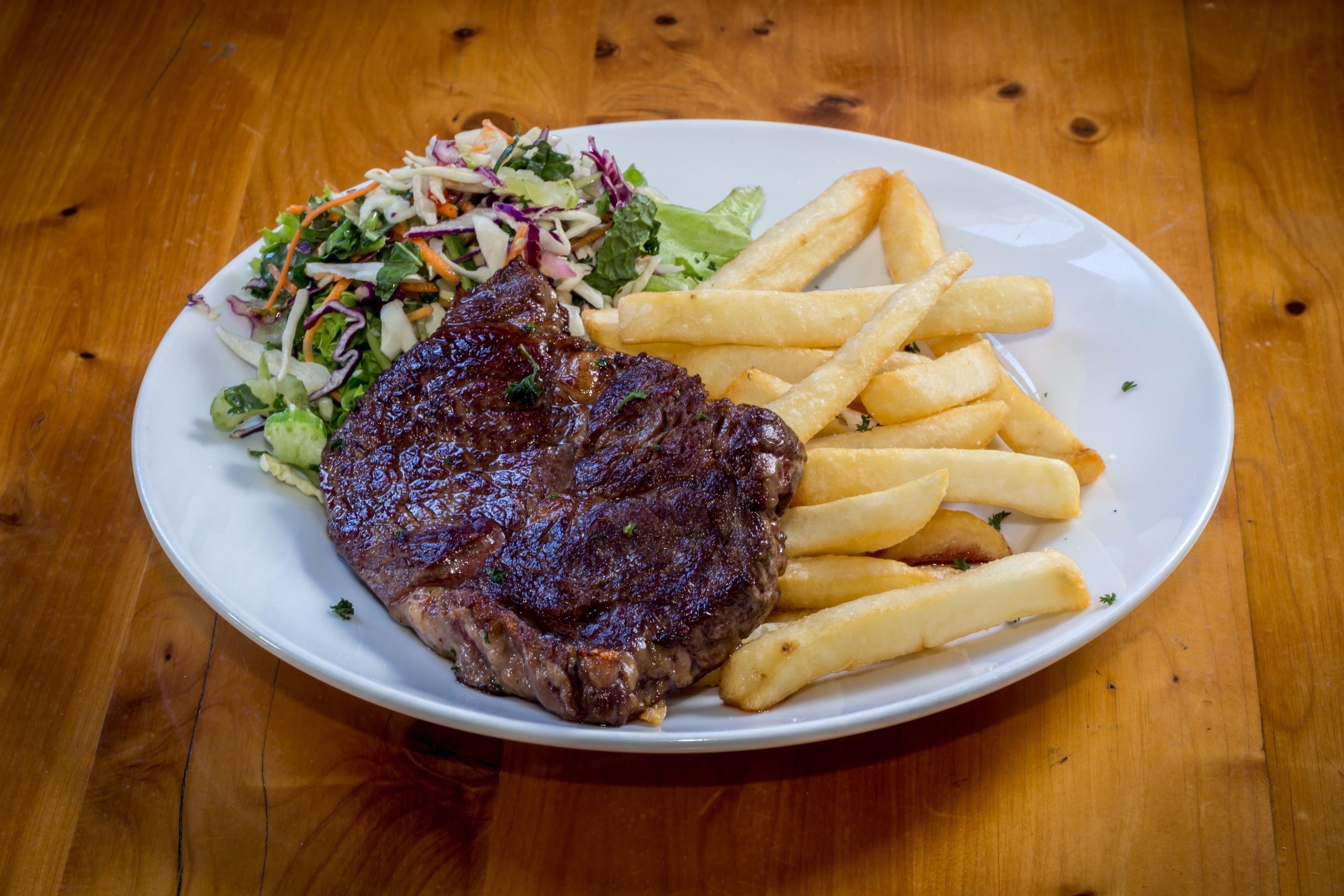 A plate with a steak, fries, and a side salad on a wooden table.