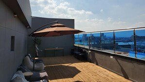 Terraza en la azotea con piso de madera, mobiliario exterior y una gran sombrilla.