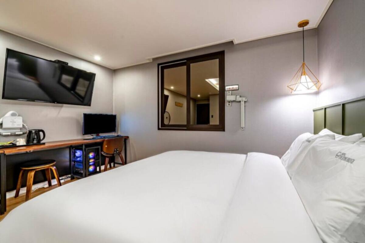 Ein Hotelzimmer mit einem Bett, einem Schreibtisch mit Computer, einem Fernseher und einem Spiegel.