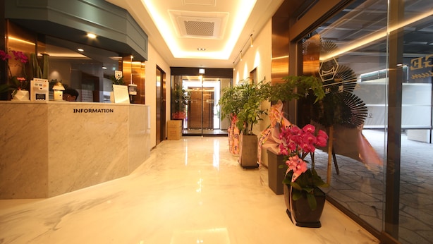 Zona de recepción de hotel con suelo de mármol, mostrador de información y plantas en macetas.