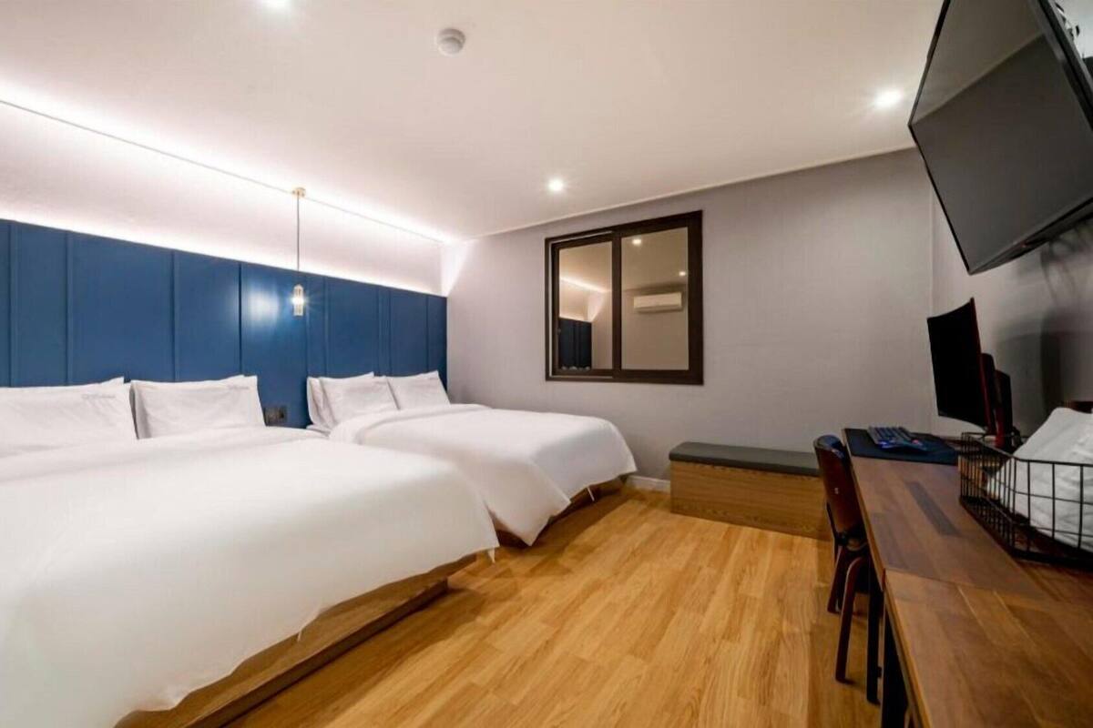Ein Hotelzimmer mit zwei Betten, einem Schreibtisch, einem Sessel, einem Fernseher und einem Spiegel.