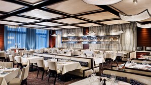 Un restaurante espacioso con varias mesas y sillas, un gran candelabro y un diseño de techo moderno.