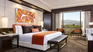 Habitación de hotel con una cama grande, un escritorio, una silla, un banco, un televisor y vistas al exterior.