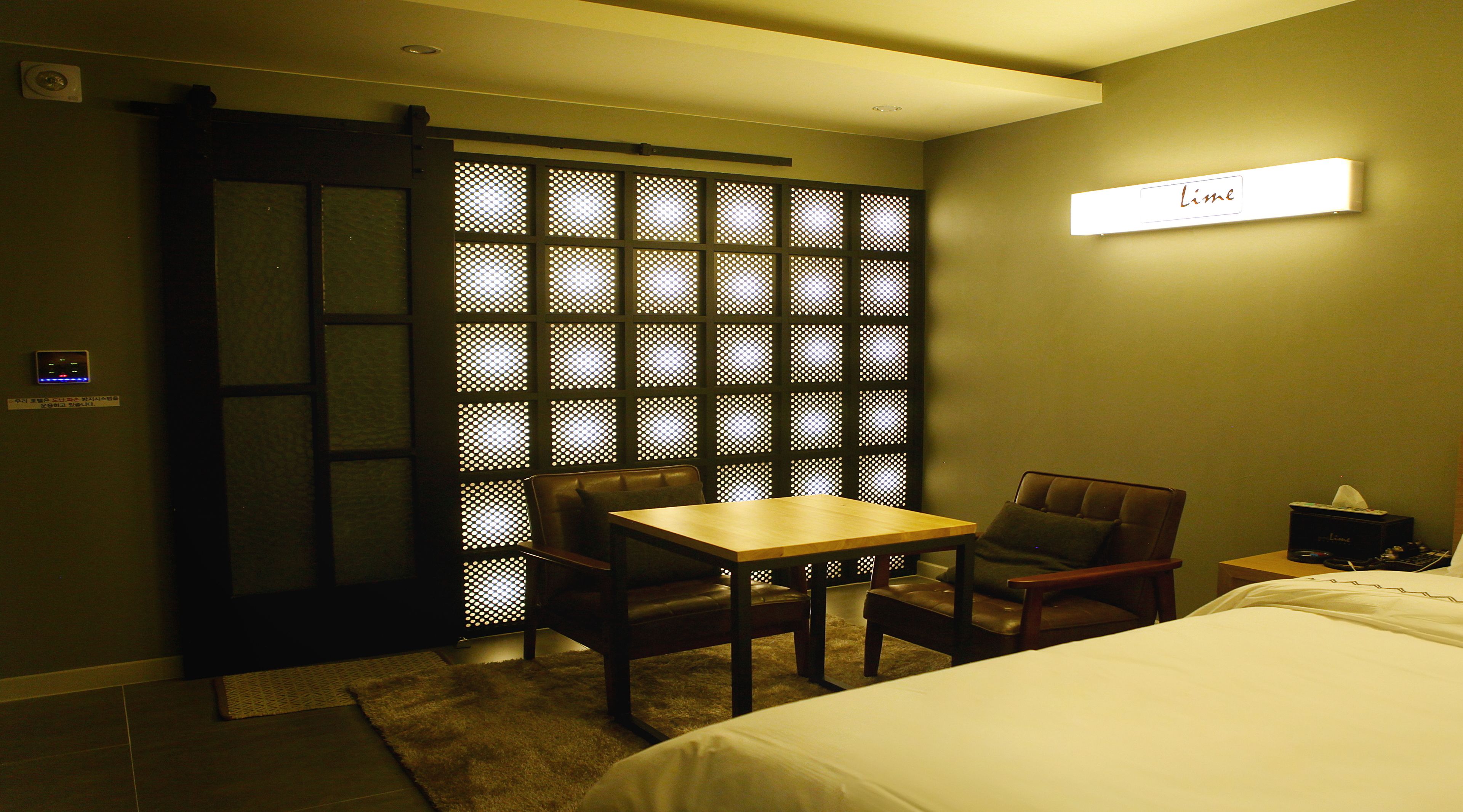 A hotel room with a bed, a table, two chairs, a small table with a tissue box, and a wall-mounted sign that says "Lime".