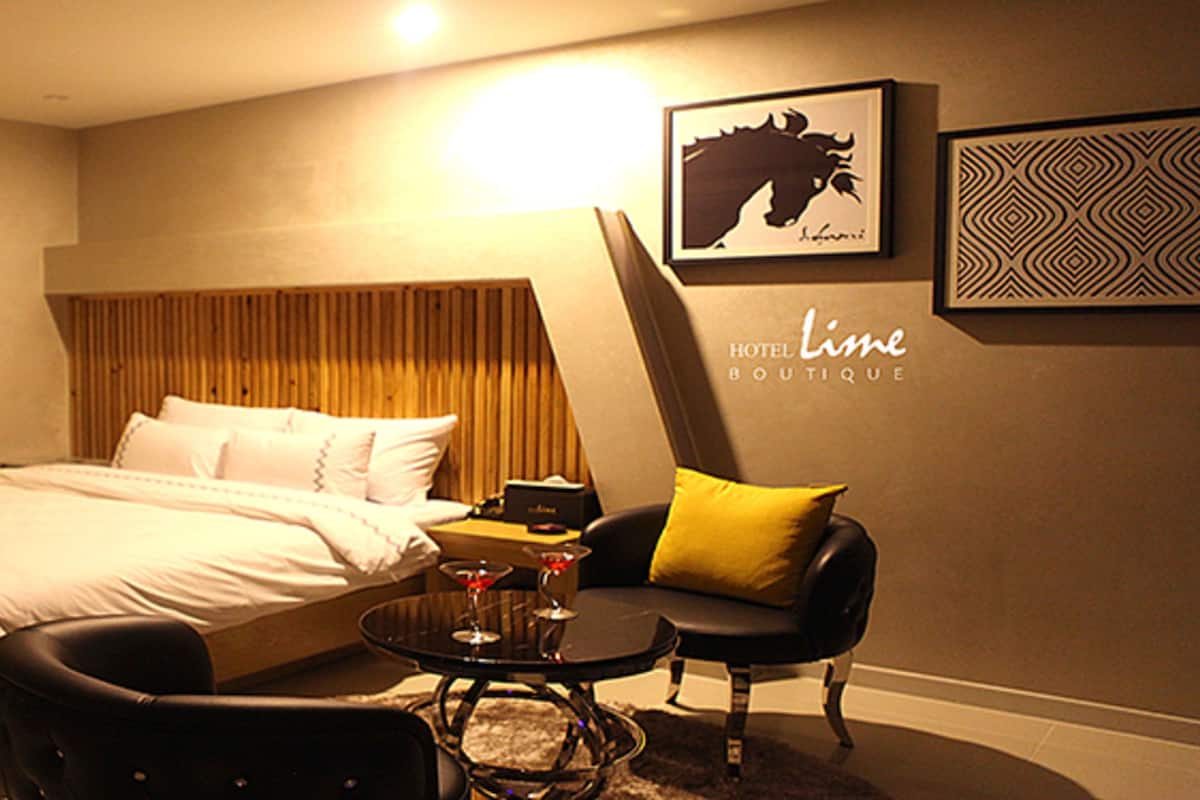 A hotel room with a bed, a chair, a small table with drinks, and artwork on the wall.