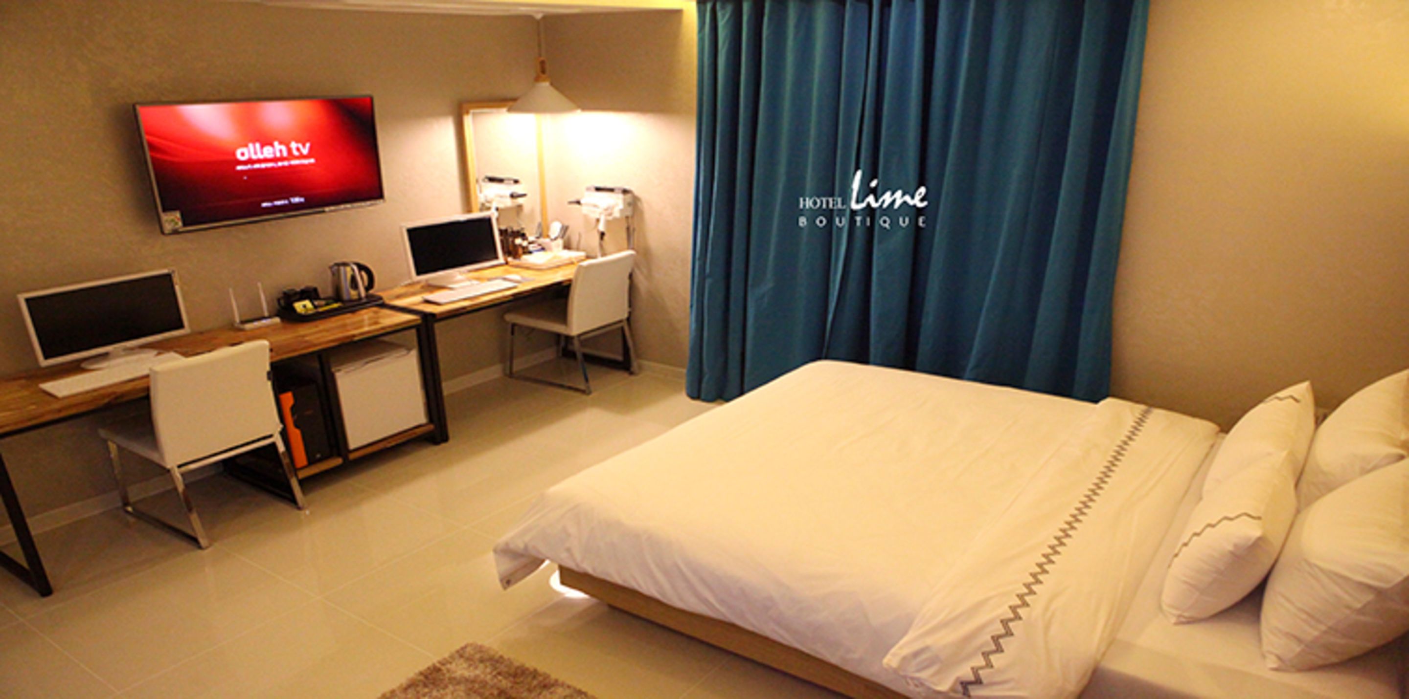 Una habitación de hotel con una cama, un escritorio con computadora, un televisor y un espejo.
