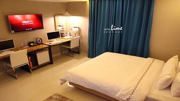 Una habitación de hotel con una cama, un escritorio con computadora, un televisor y un espejo.