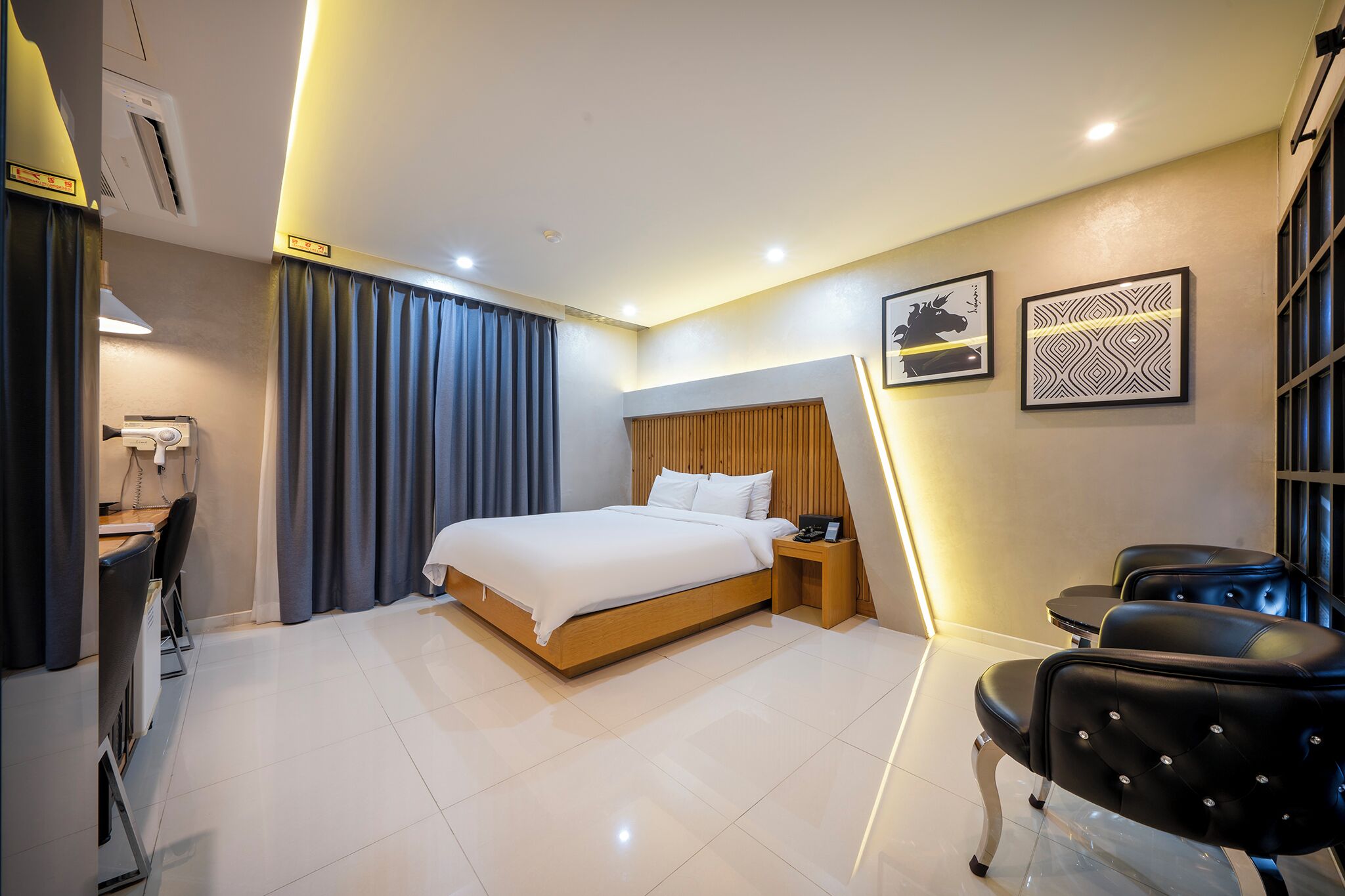Una habitación de hotel moderna con una cama grande, un escritorio con silla, una mesita y dos sillas de cuero negro.