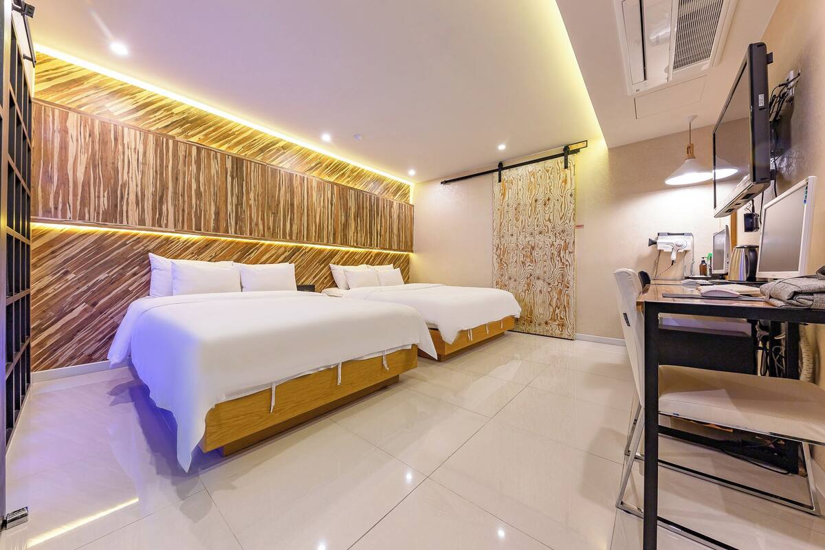 A modern hotel room with two beds, a desk, and a television.
