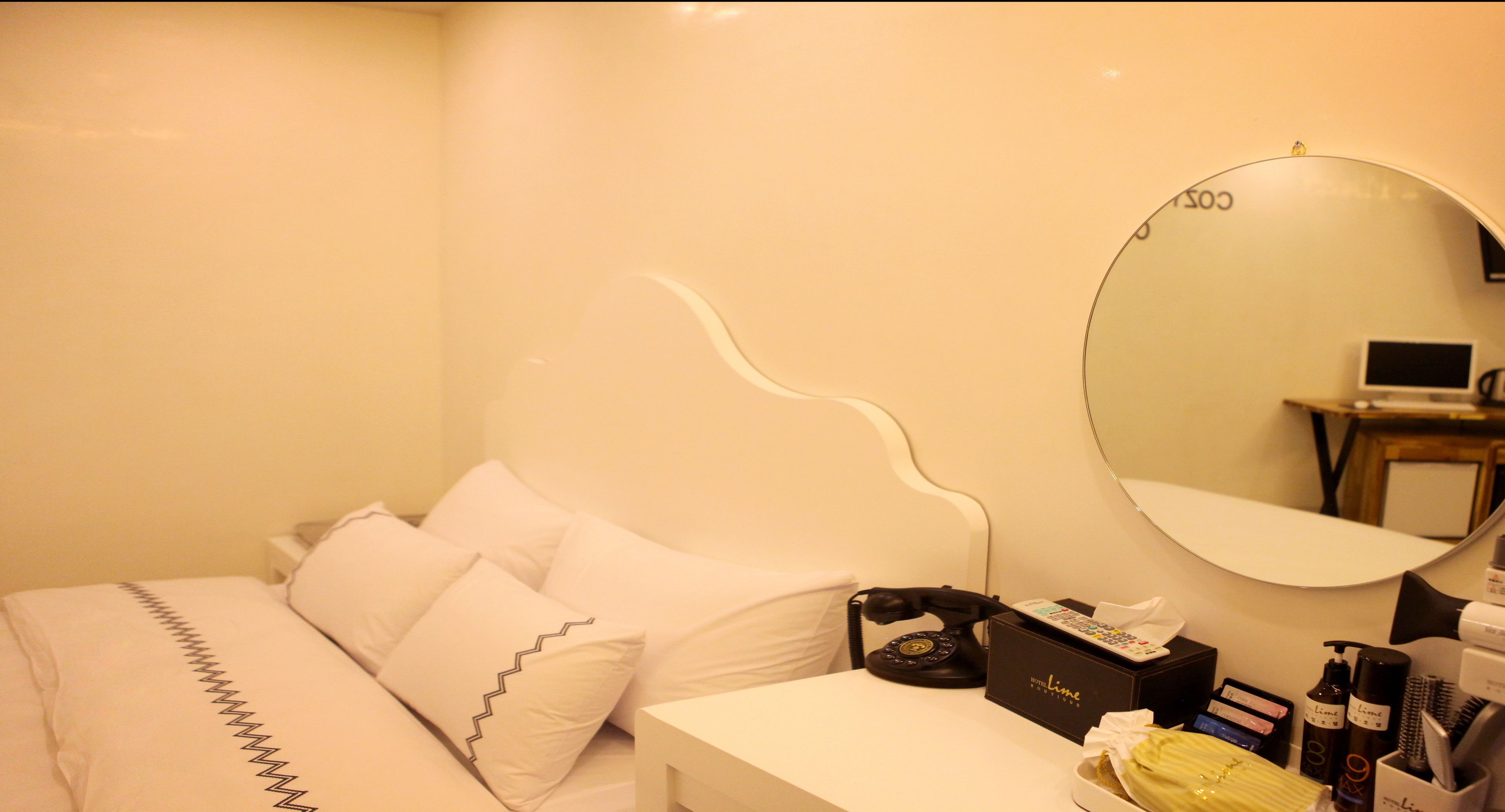 A hotel room with a bed, a bedside table with a telephone, a mirror, and toiletries.