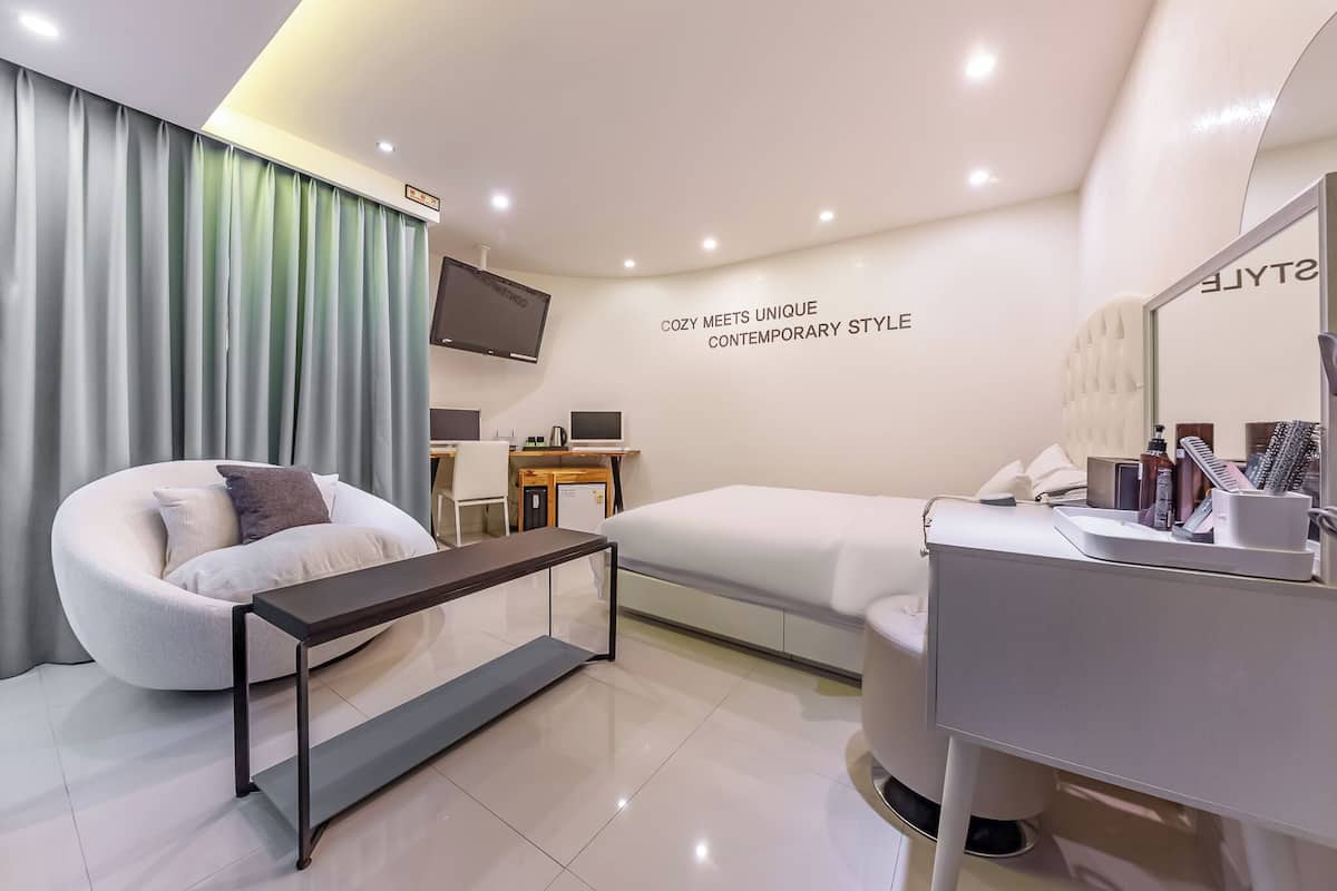 A modern hotel room with a sofa, a bed, a desk, and a TV.