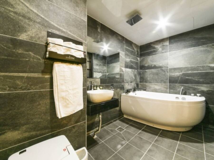 A modern bathroom with dark marble walls, a freestanding bathtub, a white sink, and a toilet.