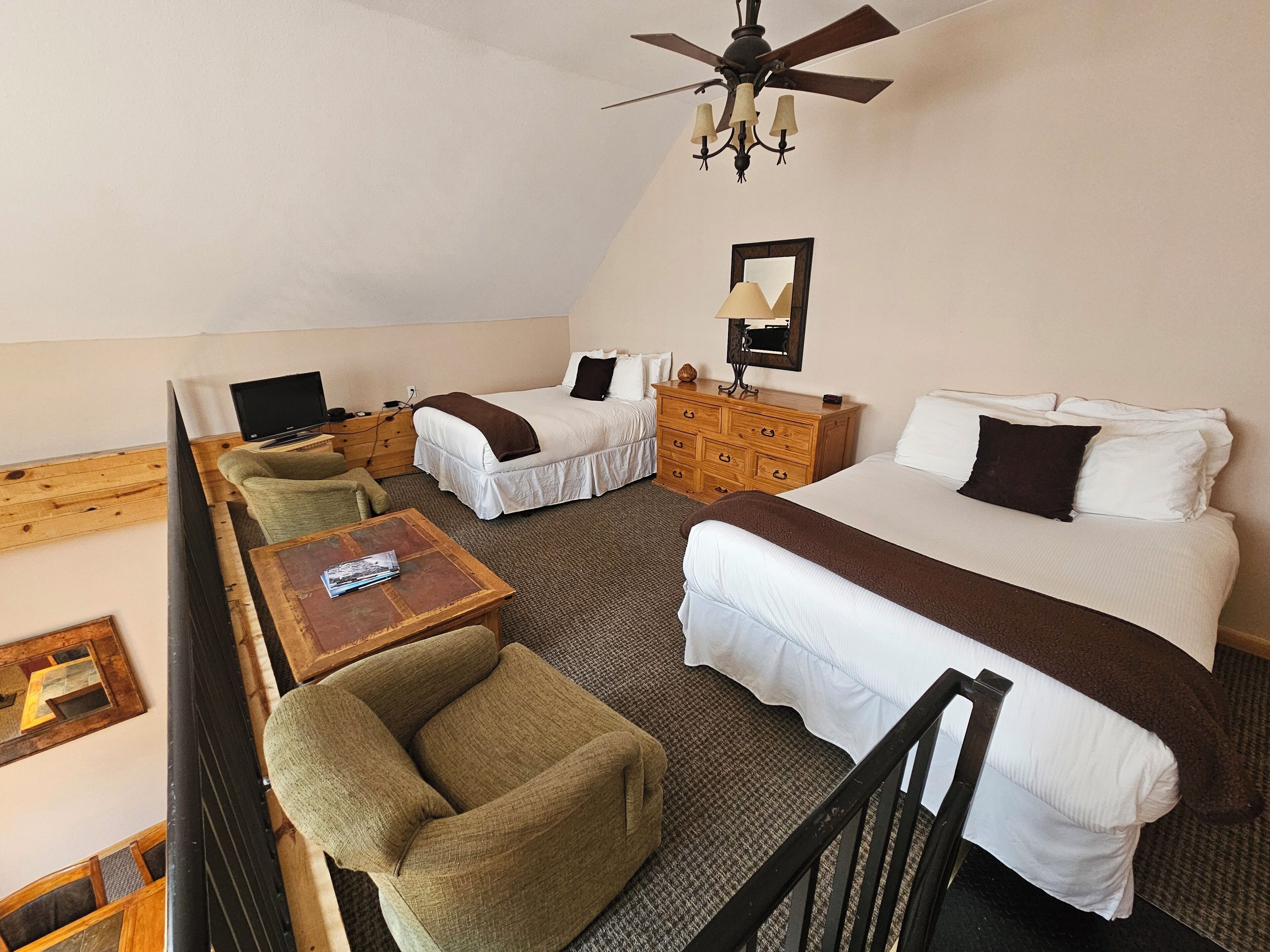 A hotel room with two beds, a wooden dresser, a television, and a ceiling fan.