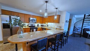 A modern kitchen with a central island, wooden cabinets, stainless steel appliances, and a spiral staircase. - Snakedance Condominiums (Taos Ski Valley)
