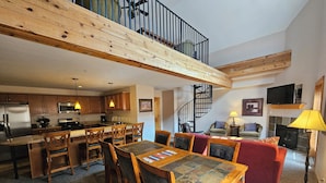 A spacious living area with a high ceiling, a dining table, and a kitchen with modern appliances. - Snakedance Condominiums (Taos Ski Valley)