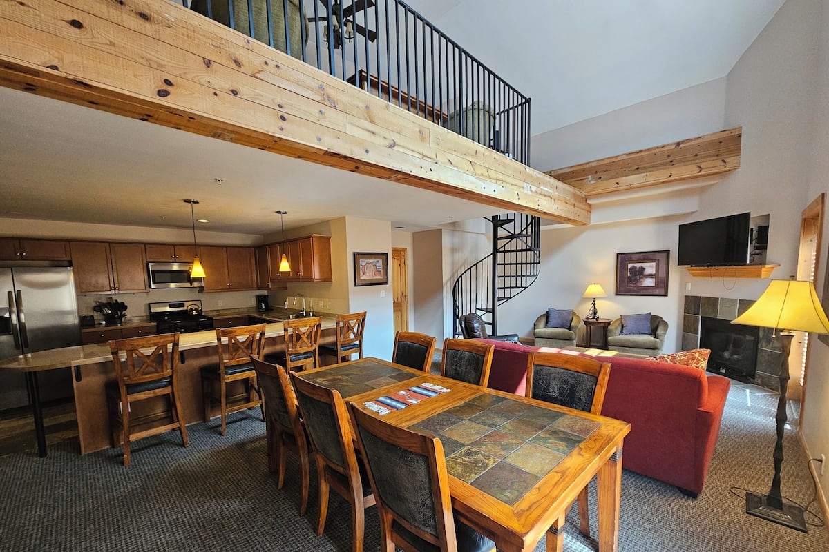 A spacious living area with a high ceiling, a dining table, and a kitchen with modern appliances.