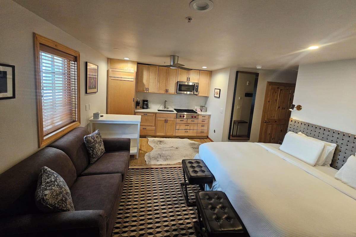 A compact hotel room with a bed, a sofa, a small kitchenette, and a bathroom.