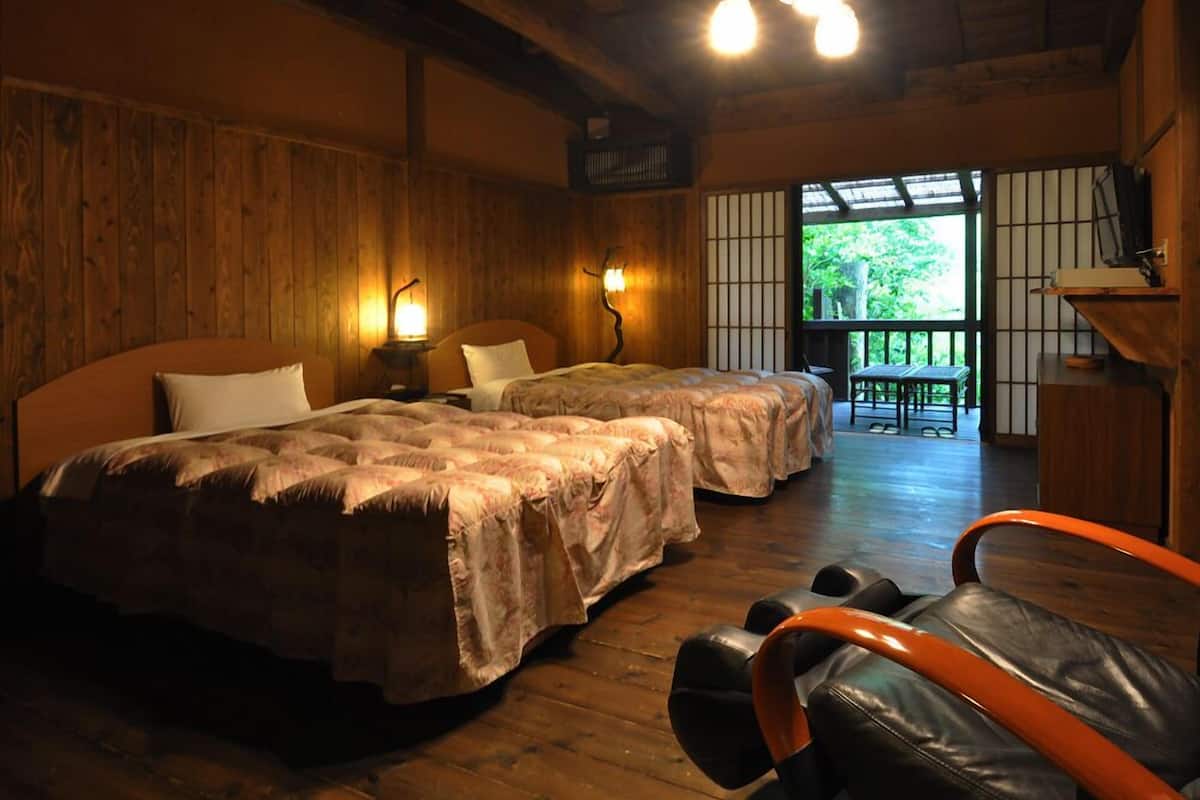 Quarto de madeira com duas camas, um banco e vista para o verde lá fora.