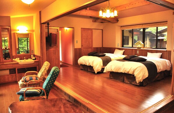 A hotel room with two beds, a sitting area with chairs, a wooden floor, a window with a view, and a chandelier.