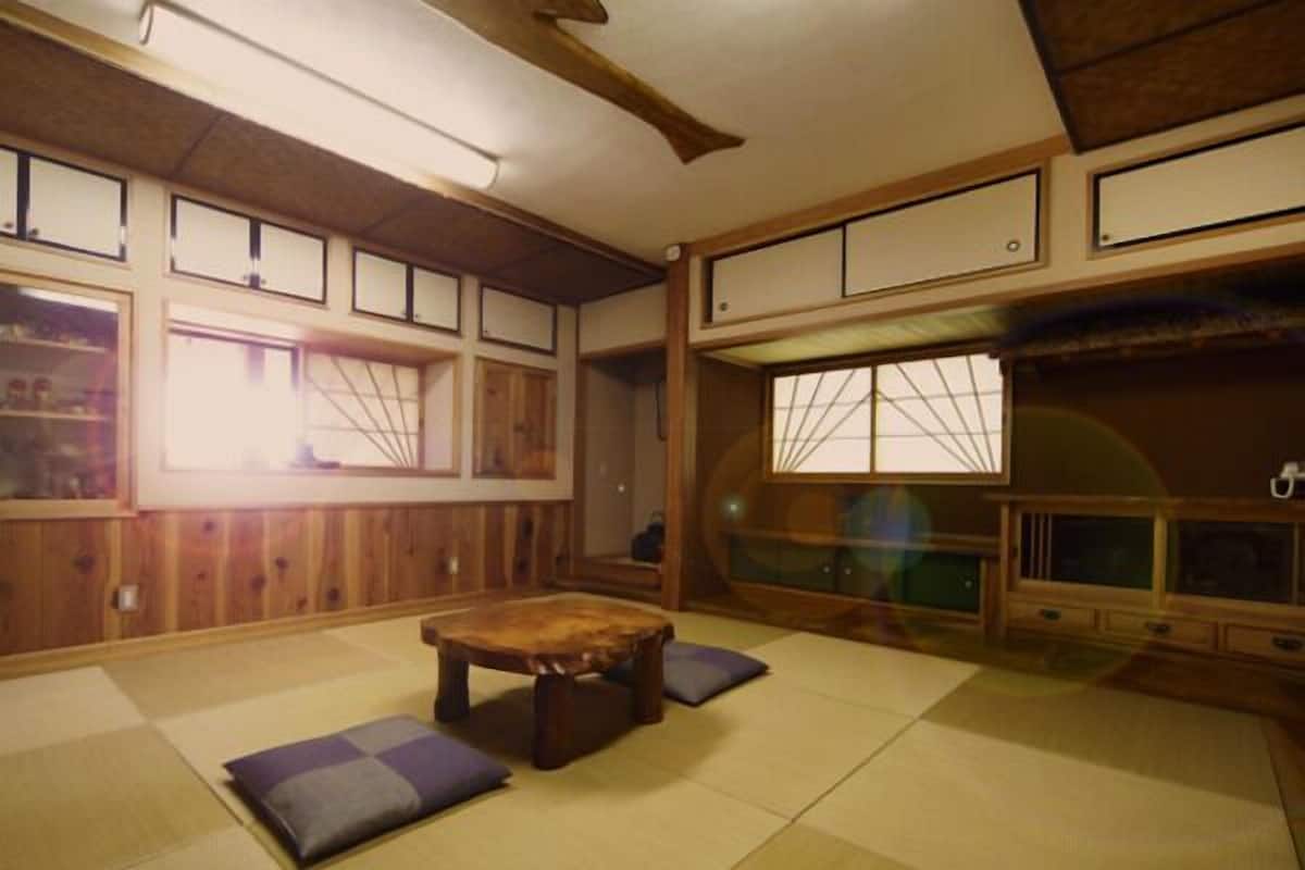 Um quarto japonês tradicional com tatames, uma mesa de madeira baixa, almofadas e portas corrediças com janelas.