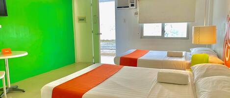 Een hotelkamer met twee bedden, een kleine tafel, een groene wand en een raam met jaloezieën.