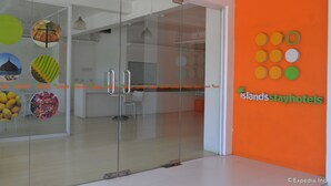 Een moderne hotellobby met een glazen scheidingswand, een receptiebalie en een feloranje wand met een circulair logo.
