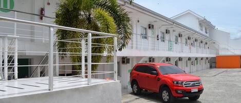 A red SUV parked in front of a building with a white facade, a palm tree, and a metal railing.