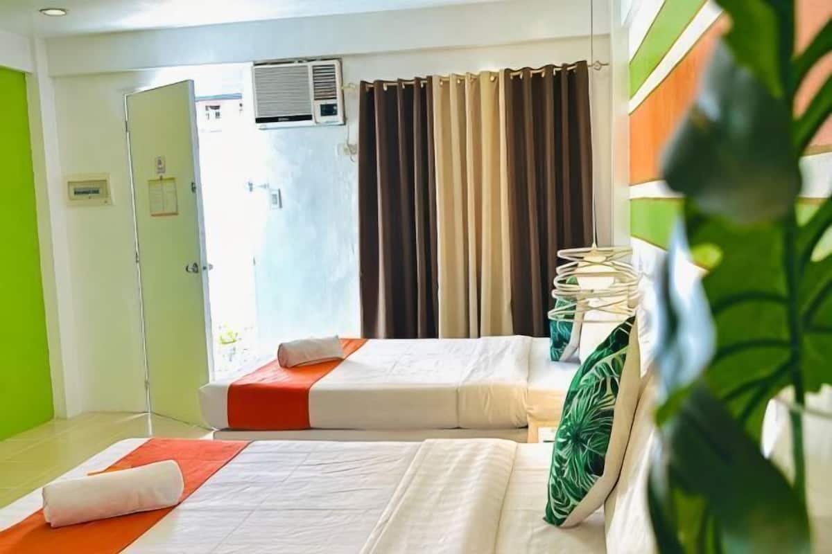 Une chambre d’hôtel avec deux lits, un mur vert, une fenêtre avec des rideaux et une plante.