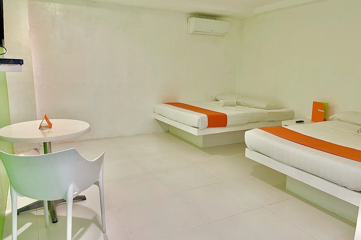 Une chambre d’hôtel avec deux lits, une petite table, une chaise et un appareil de climatisation.