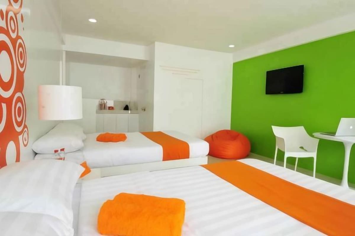 A hotel room with two beds, a green accent wall, a flat-screen TV, a small table, and a chair.