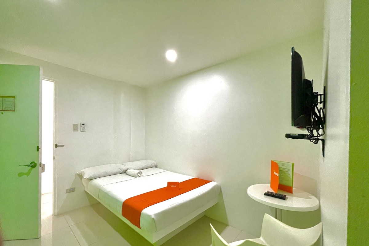 Une chambre d’hôtel avec un lit, une petite table, une chaise et un téléviseur fixé au mur.