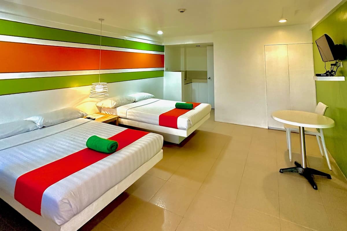 Une chambre d’hôtel moderne avec deux lits, une petite table et un mur d’accent vert.