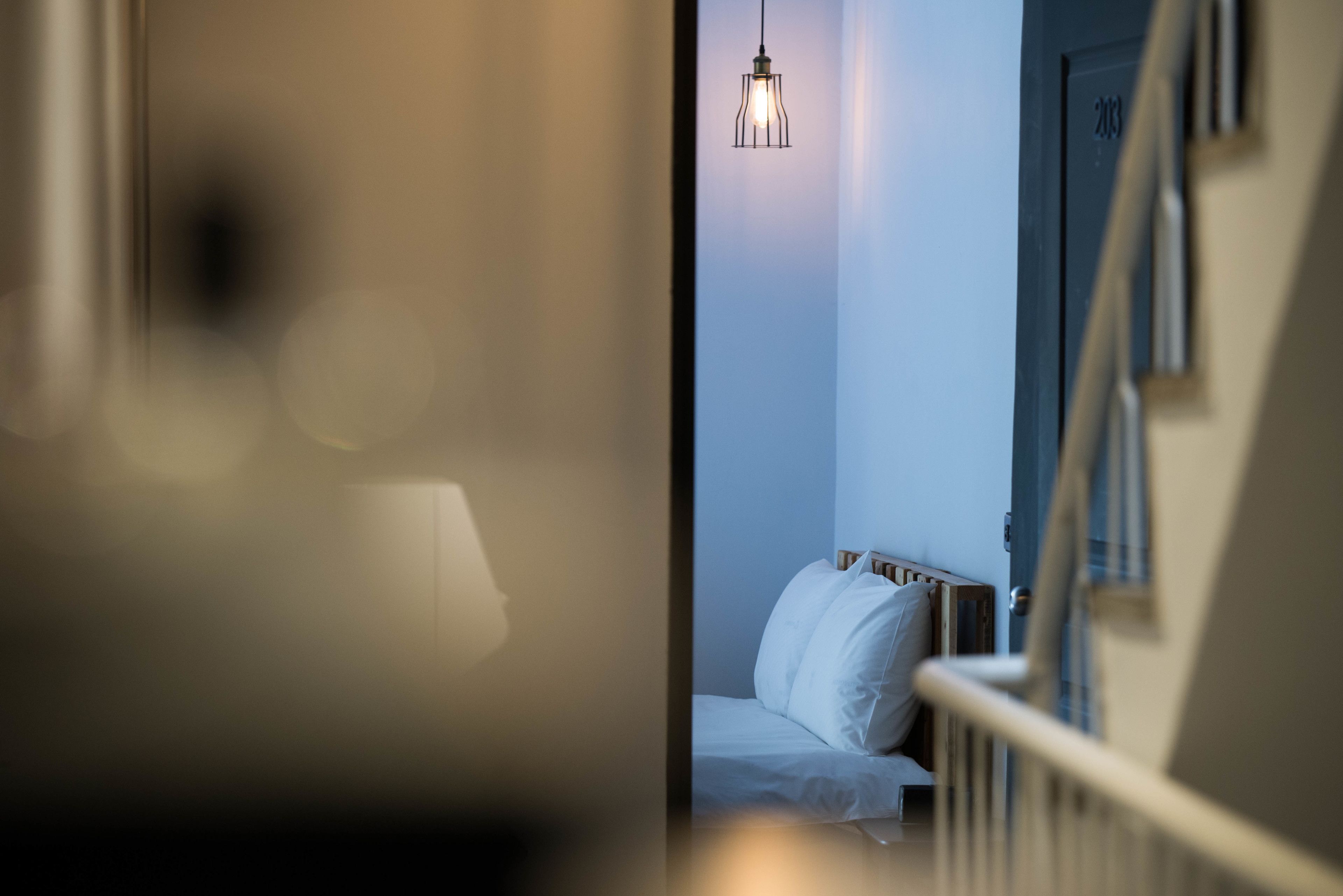 A bedroom with a bed, a hanging light fixture, and a door with a number.