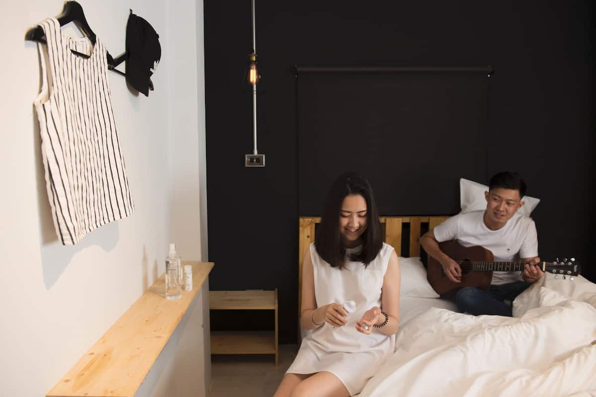 A room with a bed, a wooden nightstand, a hanging light fixture, and a wall-mounted towel rack.